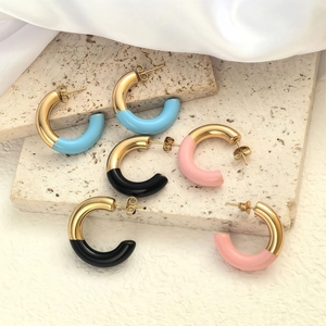 Three pairs of colorful enamel C-shape stud earrings on travertine stone with silk texture