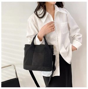 Dettaglio di una borsa tote in tela nera minimalista con manici e tracolla rimovibile