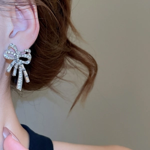 Detailed close-up of a silver bow earring with shimmering clear crystals worn by a model