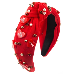 Détail d'un serre-tête noué rouge avec perles, cristaux et breloques en cœur