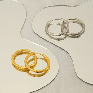 Detail of textured hoop earrings in gold and silver with rhombus engraved patterns