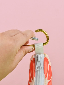 Detail of a grapefruit-shaped pet waste bag dispenser with a golden metal hook and pink zipper