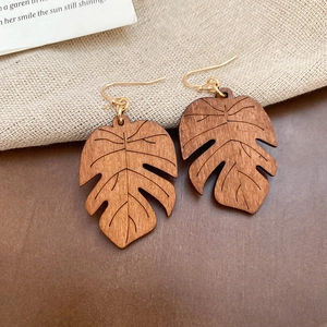 Macro shot of brown wooden Monstera leaf earrings with golden hooks on burlap background
