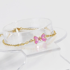 Elegant gold chain bracelet featuring a pink cubic zirconia bow on a jewelry stand