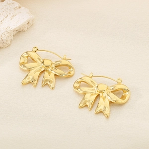 Detail of 18K gold-plated stainless steel bow earrings on a beige textured background