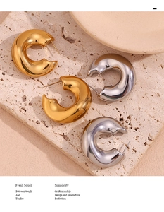 Close-up of polished gold and silver C-shaped teardrop earrings on a stone slab