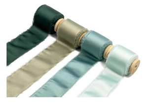 Détail de rubans en mousseline effilochée vert et bleu sur des bobines en bois
