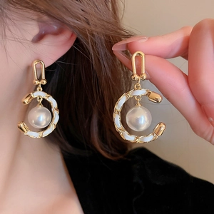 Detailed view of pearl earrings with woven leather gold chain hoops on model's ear