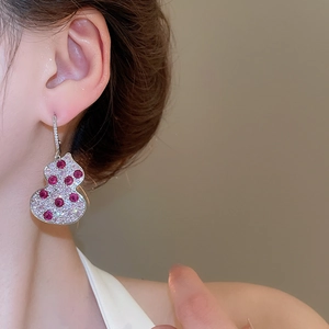 Detailed close-up of a silver gourd earring with red gemstones and pavé-set zircons on model