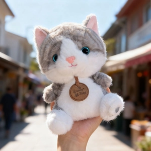 Cute gray and white plush cat toy with blue eyes held by a hand in outdoor sunlight
