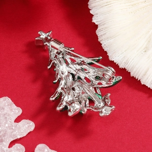 Back view of silver Christmas tree brooch with green enamel details on red backdrop