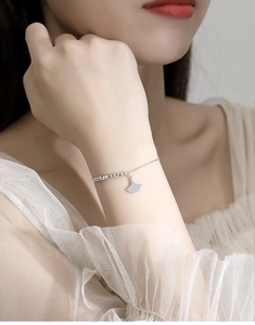 Macro side view of a S925 silver ginkgo leaf bracelet worn on a female wrist with lace