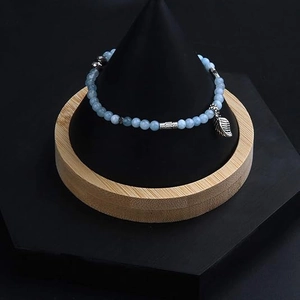Detailed close-up of light blue gemstone beads with a silver metal leaf pendant charm