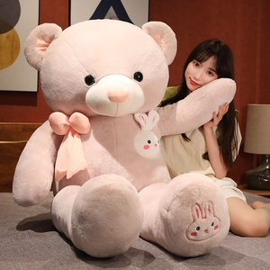 Close-up of a pink plush teddy bear with a white bunny detail and a pink ribbon bow
