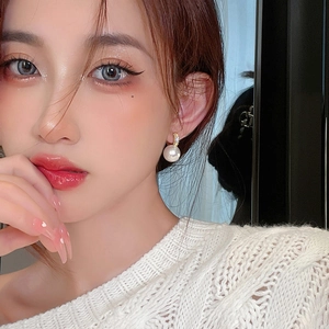 Elegant gold earrings with a large round white pearl and diamond accents on model