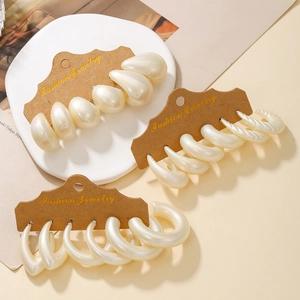 Detailed view of pearlescent white hoop earrings in drop and twisted styles on a display card