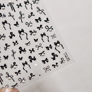 Detail of 3D nail art stickers featuring black bows with white pearls and sparkling crystals