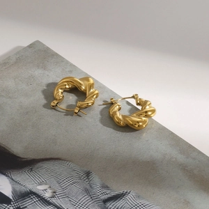 Detail of gold-plated stainless steel twist hoop earrings on minimalist background