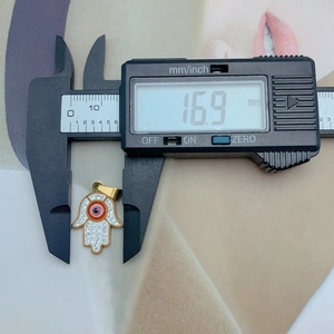 Macro view of gold Hamsa pendant width measurement showing 16.9mm on digital caliper