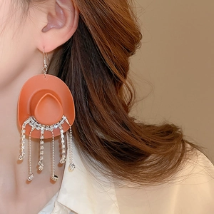 Detail of orange cowboy hat earrings with sparkling rhinestone tassels on model