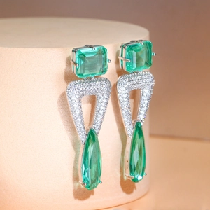 Macro detail of geometric silver earrings with green stones and sparkling pavé accents