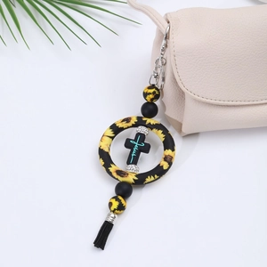 Detail of a black silicone cross car charm with sunflower beads and tassel on a bag