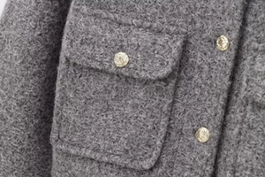 Detail of grey bouclé jacket featuring elegant gold buttons and textured fabric pocket