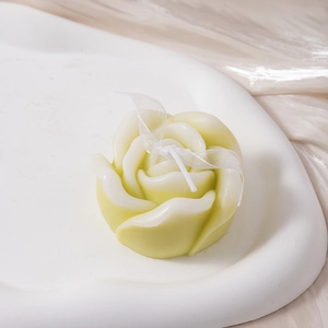 Detailed view of rose-shaped cream candle decorated with a white mesh ribbon on a stone tray