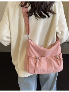 Pink pleated nylon crossbody bag with adjustable strap worn by model in a minimal setting