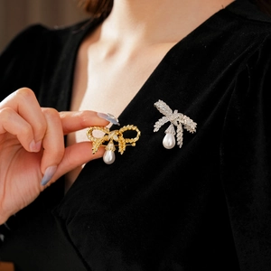 Détail d'une élégante broche nœud doré avec perle goutte sur un vêtement en velours noir