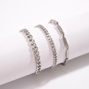 Three silver stainless steel chain bracelets displayed on a minimalist white cylinder
