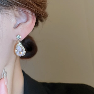 Detail of elegant gold teardrop earrings with central crystal and surrounding small diamonds