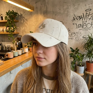 Distressed cream baseball cap with AB embroidery and ripped details in outdoor cafe setting