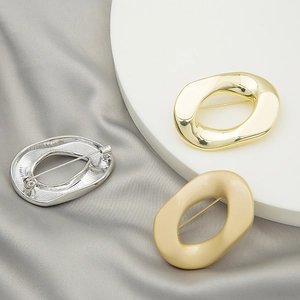 Detailed view of irregular geometric brooches in gold, silver, and matte cream finish