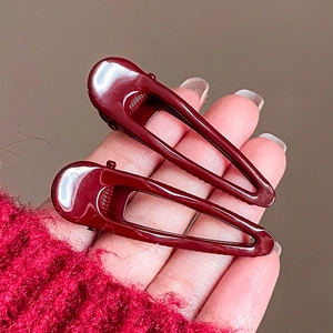 Detail view of two glossy wine red geometric hair clips with a hollow teardrop design