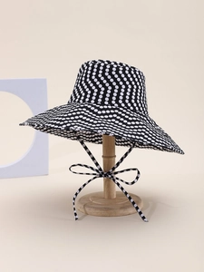 Close-up of black sun hat with white polka dots featuring a decorative bow tie and wide brim
