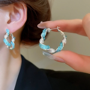 Détail de créoles torsadées en argent avec cristaux bleu clair portées par un mannequin