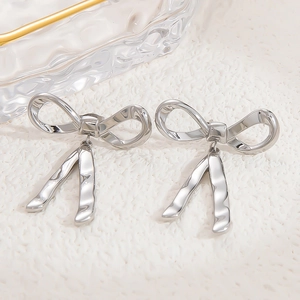 Macro close-up of silver bow earrings with a polished mirror finish on white texture