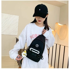 Détail du sac de poitrine en toile noire avec un pendentif mouton blanc et logo