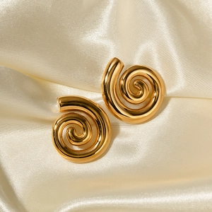 Detail of gold spiral hoop earrings on elegant beige satin fabric with soft highlights