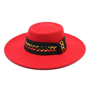 Detail of red wide-brim felt fedora hat featuring black ribbon and gold metal chain link