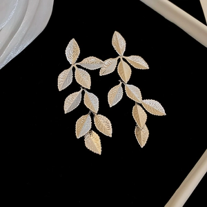 Macro detail of golden leaf drop earrings with intricate vein textures on black background