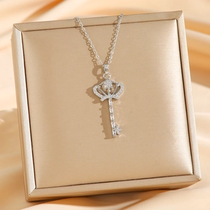 Collier clé couronne en argent avec détails étoiles et pavé de cristaux sur boîte dorée