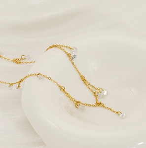 Close-up of golden fringe necklace with clear zircon charms on white porcelain edge