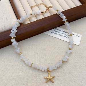 Macro detail of white opal stone necklace with a gold starfish pendant on burlap