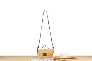 Detail of beige woven straw crossbody bag with brown leather strap and metal clasp