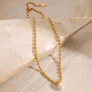 Détail d'un collier en or avec pendentif perle posé sur une pierre texturée beige