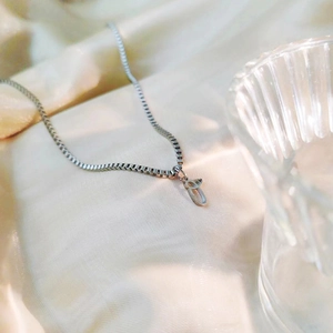 Gros plan du pendentif lettre cursive sur soie beige avec verre strié élégant
