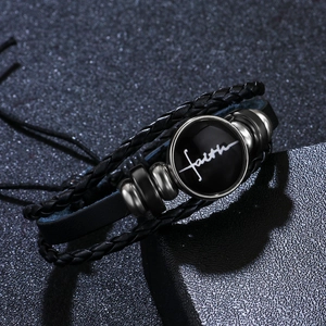 Multilayer black woven leather bracelet with polished faith charm on dark background