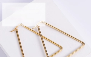 Close-up of golden geometric triangle earrings on a minimalist white display stand
